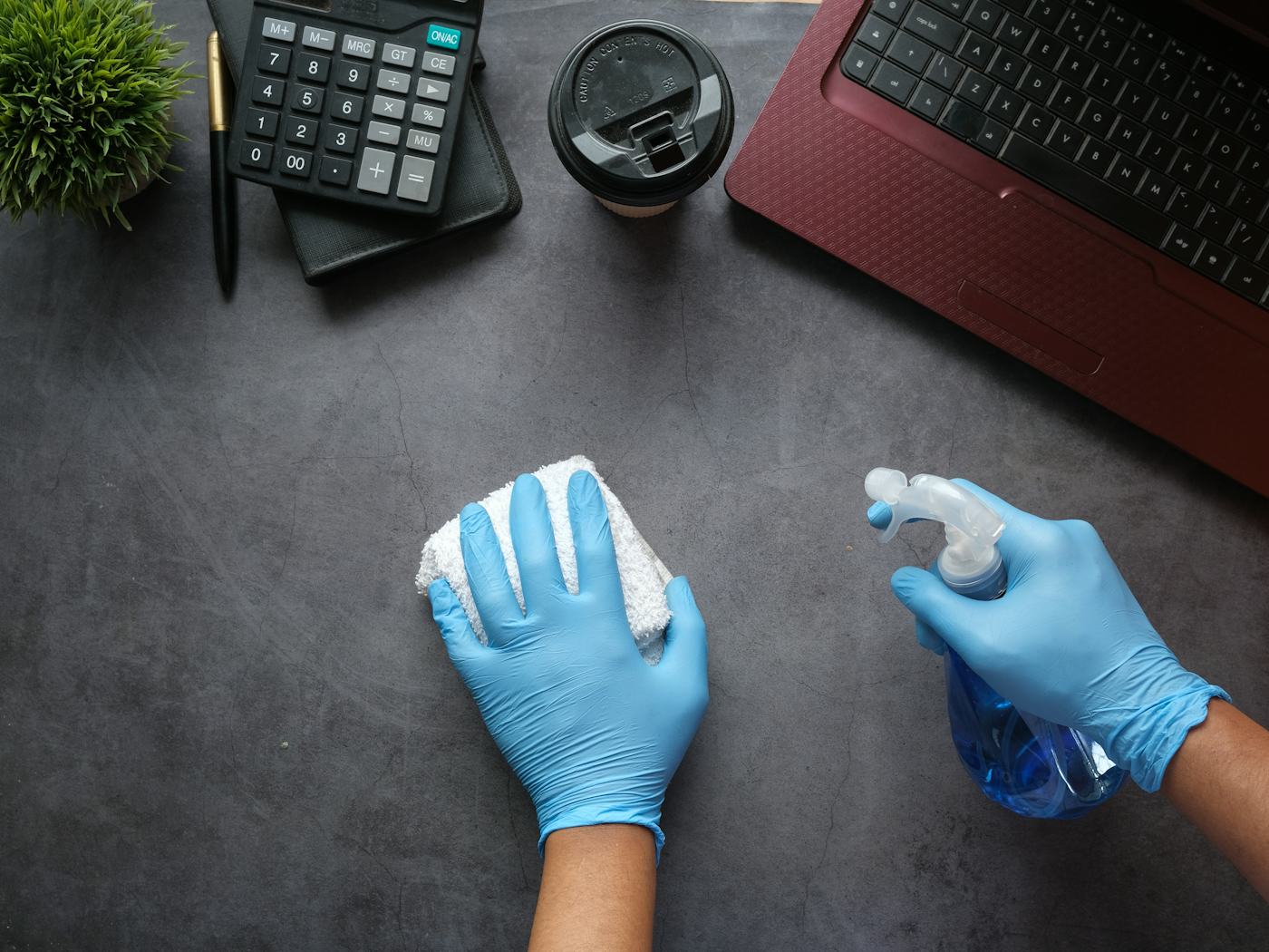 Hände in Schutzhandschuhen reinigen eine Schreibtischplatte